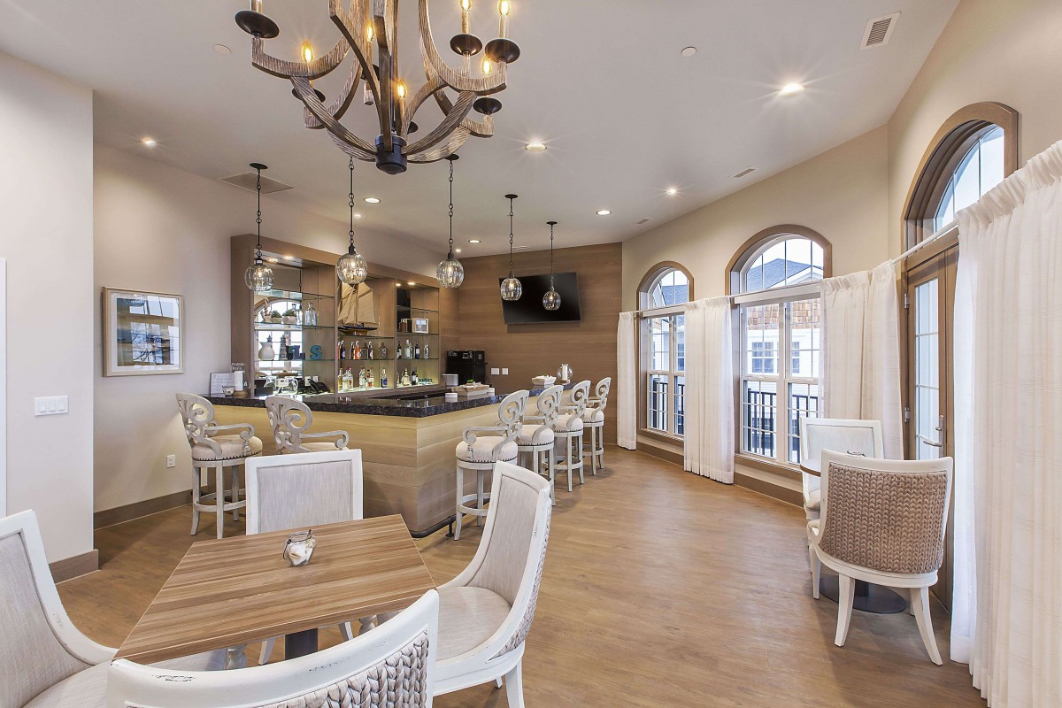 A modern restaurant interior featuring a dining area with tables and chairs, a bar, and decorative chandeliers.