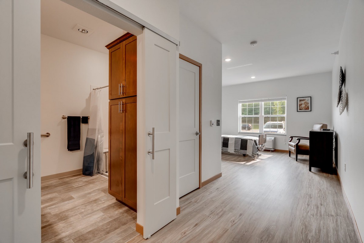 A modern interior featuring a bedroom and adjacent bathroom with hardwood flooring and ample natural light.