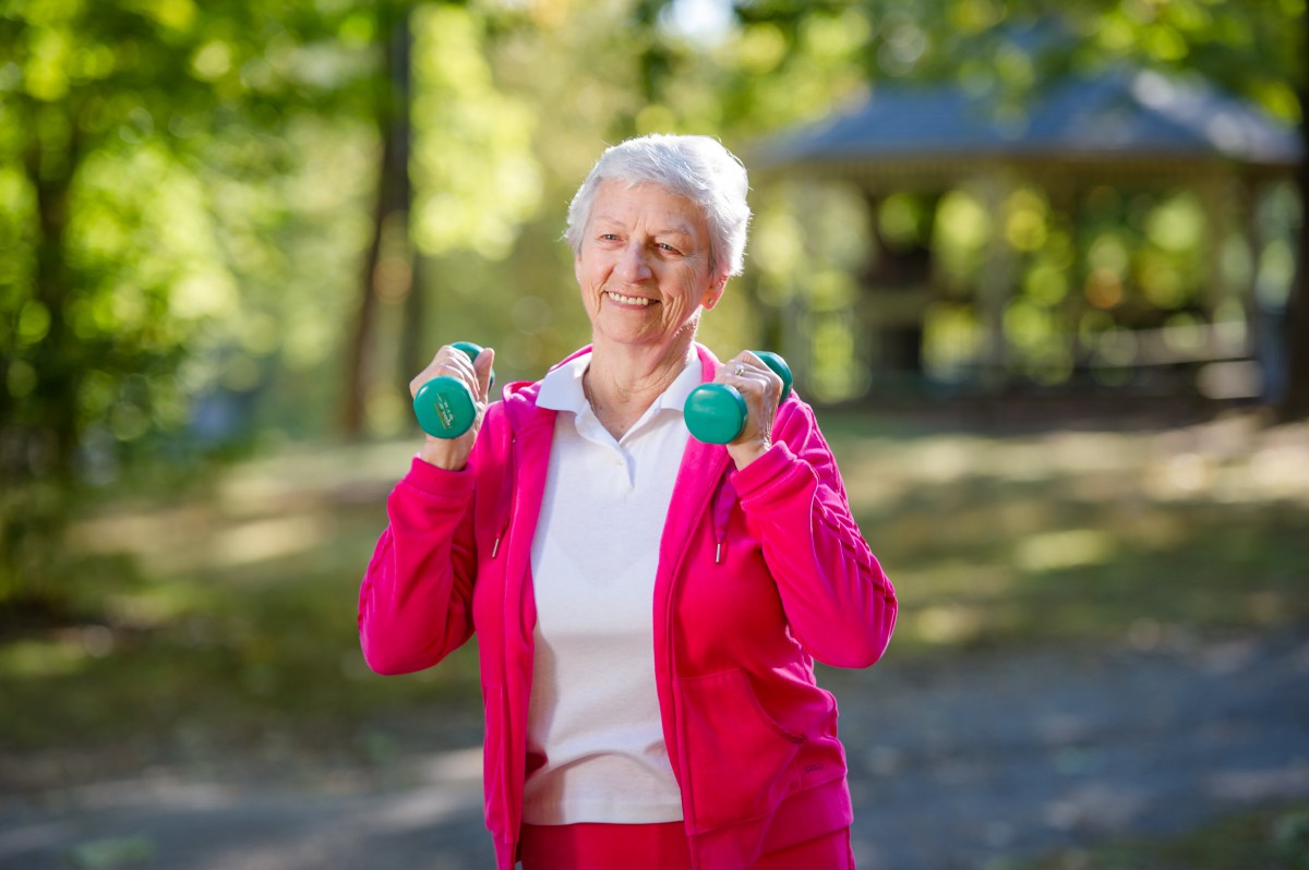 An elderly woman exercising with small dumbbells outdoors.