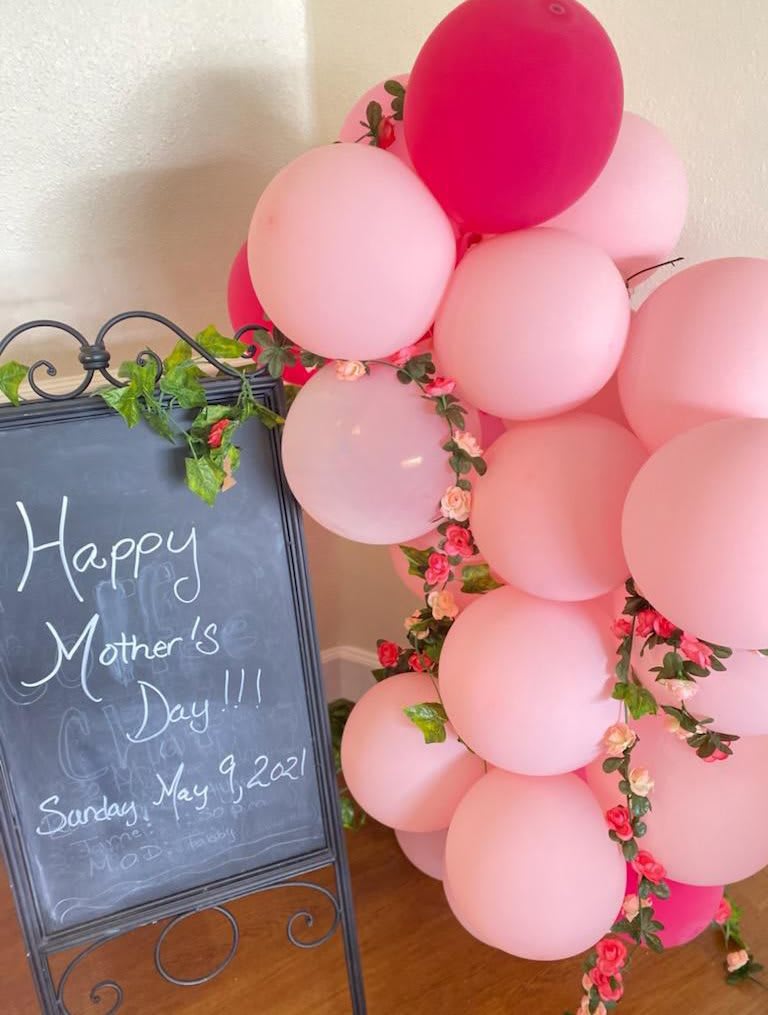 A festive Mother's Day decoration with pink balloons and a chalkboard sign.
