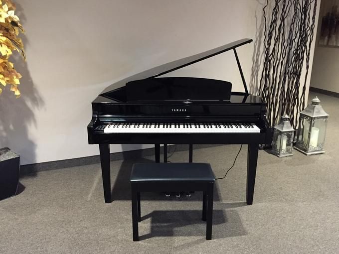 A sleek black digital grand piano with a matching bench in a minimalist music room.