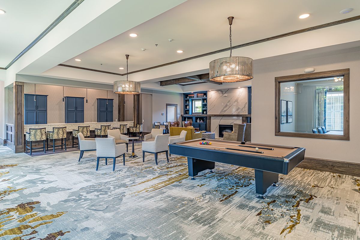 A modern game room featuring a pool table, spacious seating area, and stylish chandeliers.
