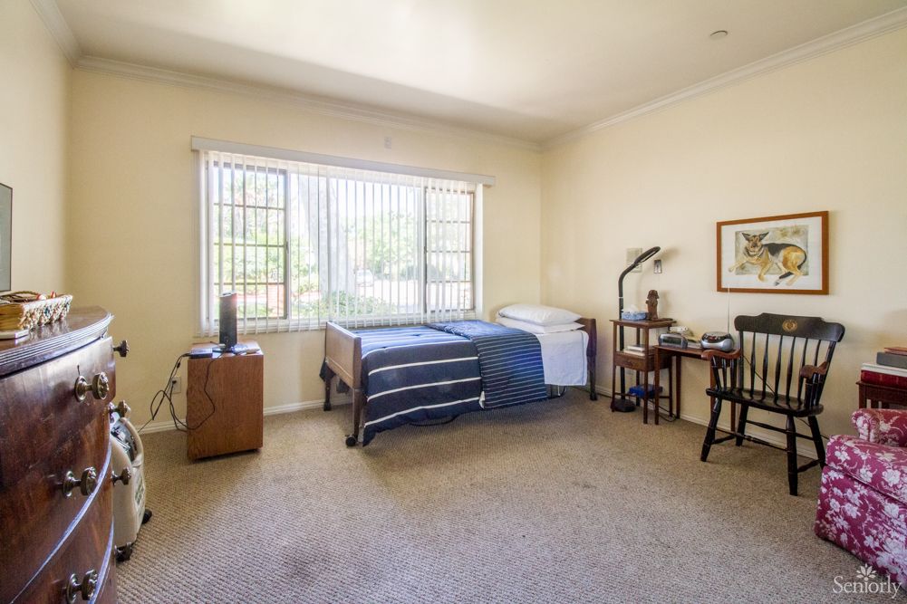 A simple bedroom with a bed, desk, and window offering natural light.