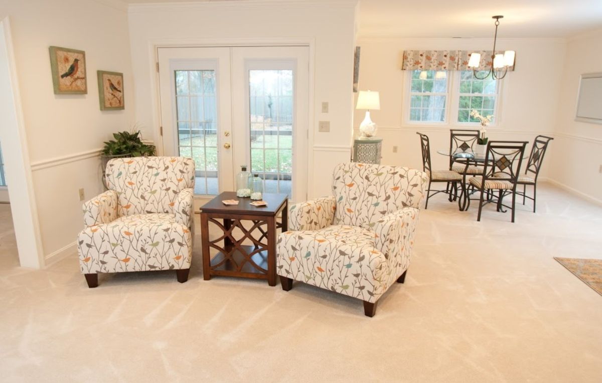 A cozy living room with two patterned armchairs, a wooden coffee table, and large windows in the background.
