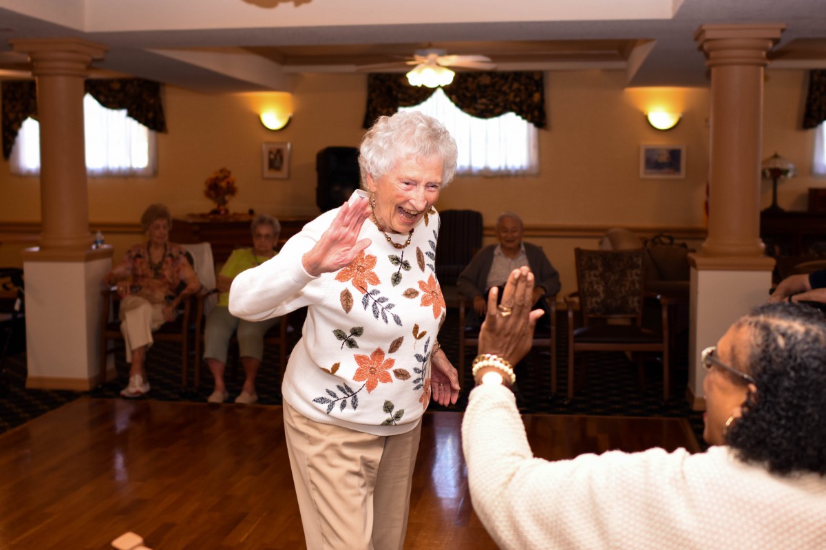 Elderly woman dancing and enjoying a social event indoors.
