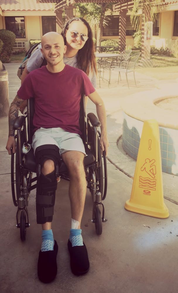 A person in a wheelchair with a knee brace, outdoors near a caution sign.