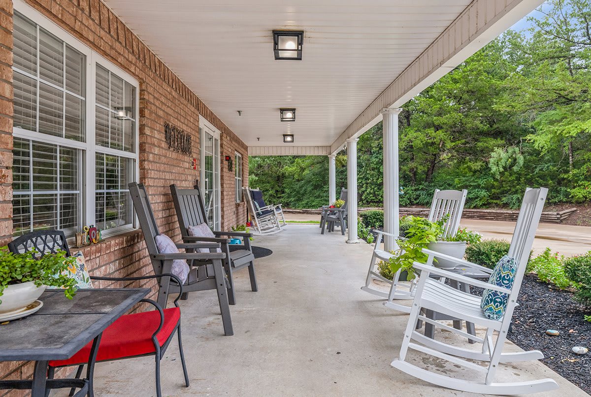 A spacious covered porch with various chairs, including rocking chairs, alongside a brick wall.