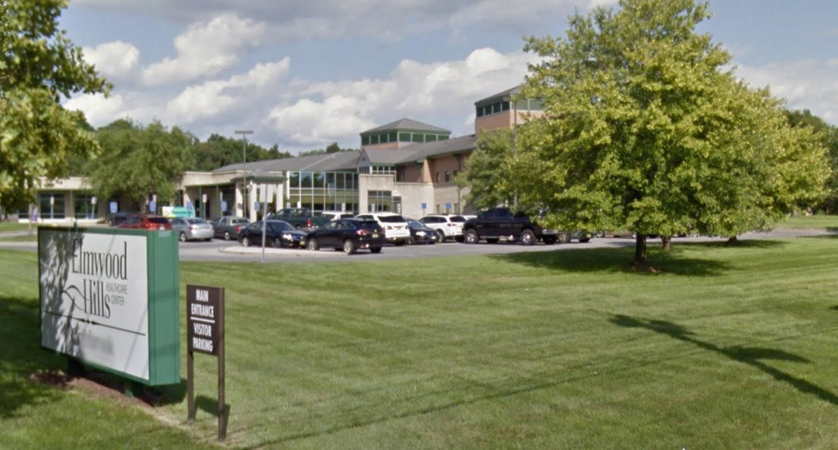 A view of a modern building with cars parked in front and a green lawn.