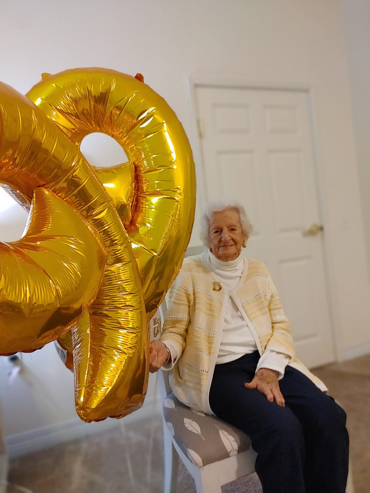 An elderly person is celebrating a birthday with gold number balloons indoors.