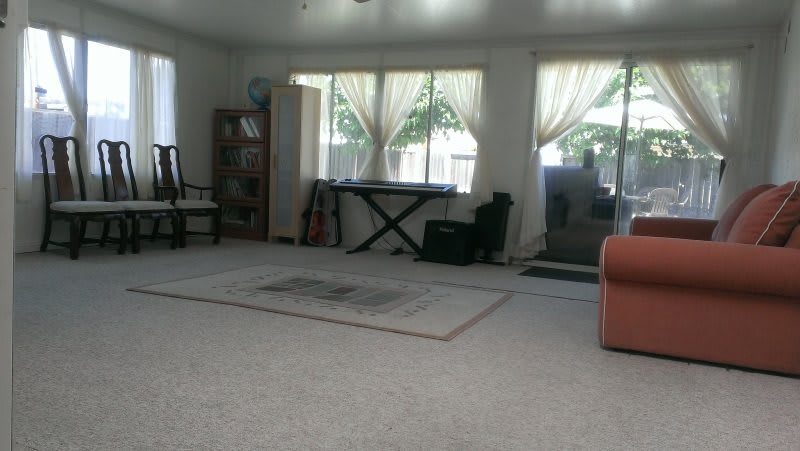 A spacious living room with a piano, bookshelf, and large windows letting in natural light.