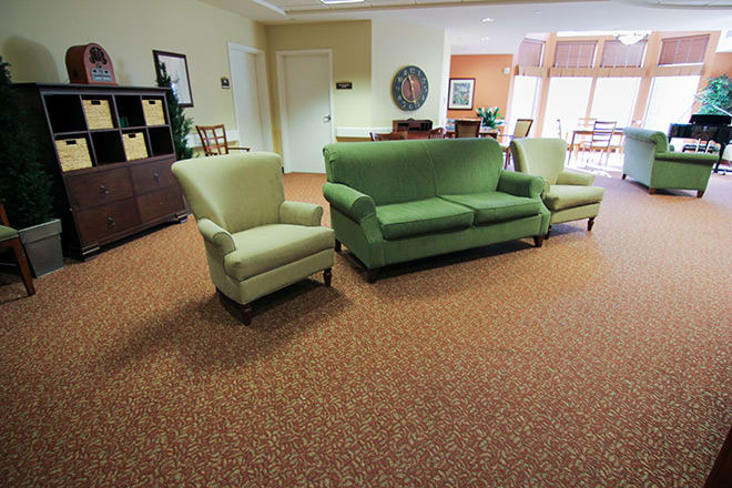 A cozy living room with a green sofa and armchairs on a brown carpet.