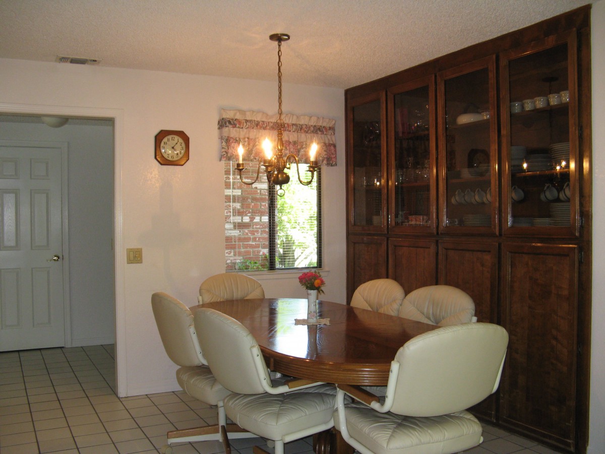 A dining room with a wooden table, upholstered chairs, and a chandelier under natural light from the window.