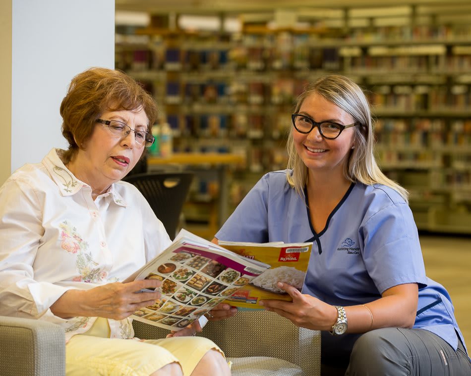 A nurse and an elderly woman reading a magazine together in a library setting.