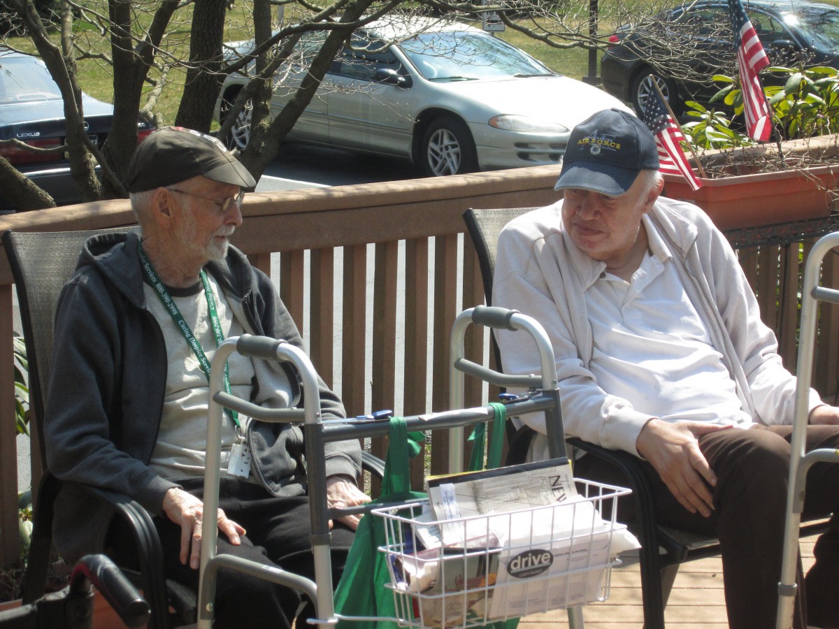 Two elderly men sitting on a porch, engaged in conversation and enjoying the outdoors.