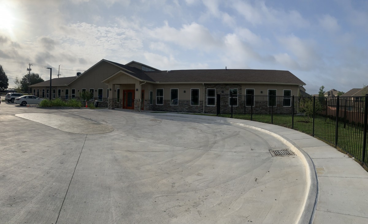 A single-story building with a wide driveway and a cloudy sky overhead.