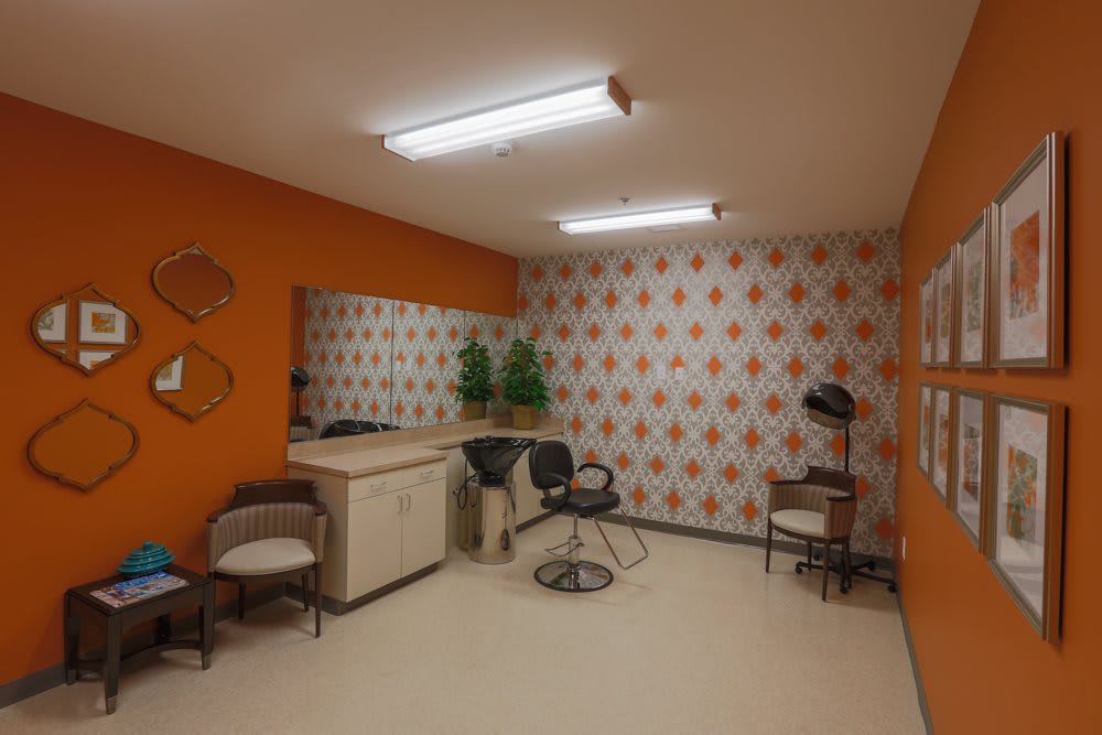 A retro-themed hair salon with orange walls and patterned wallpaper, featuring a vintage hairdryer and chairs.