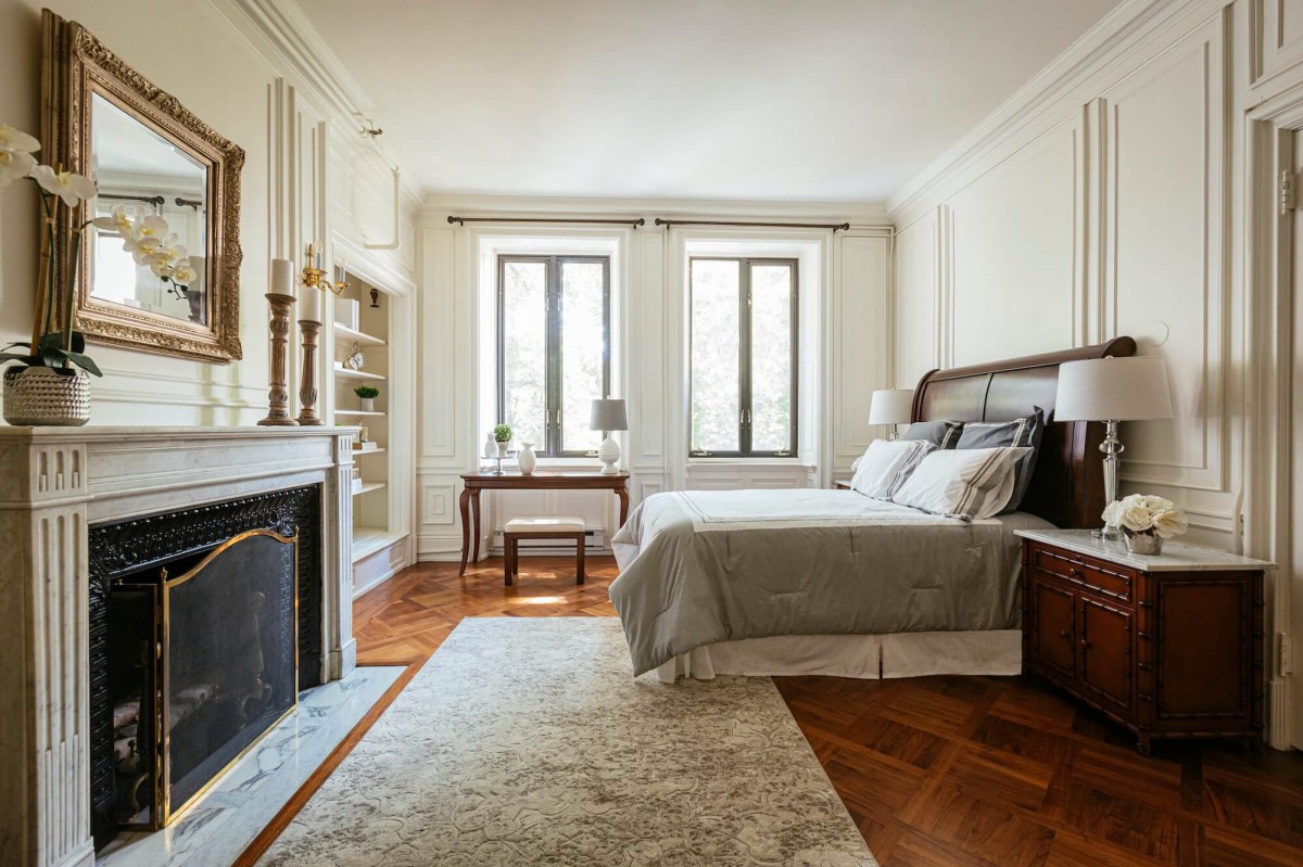 A well-decorated bedroom with a cozy ambiance, featuring a bed, fireplace, and large windows.