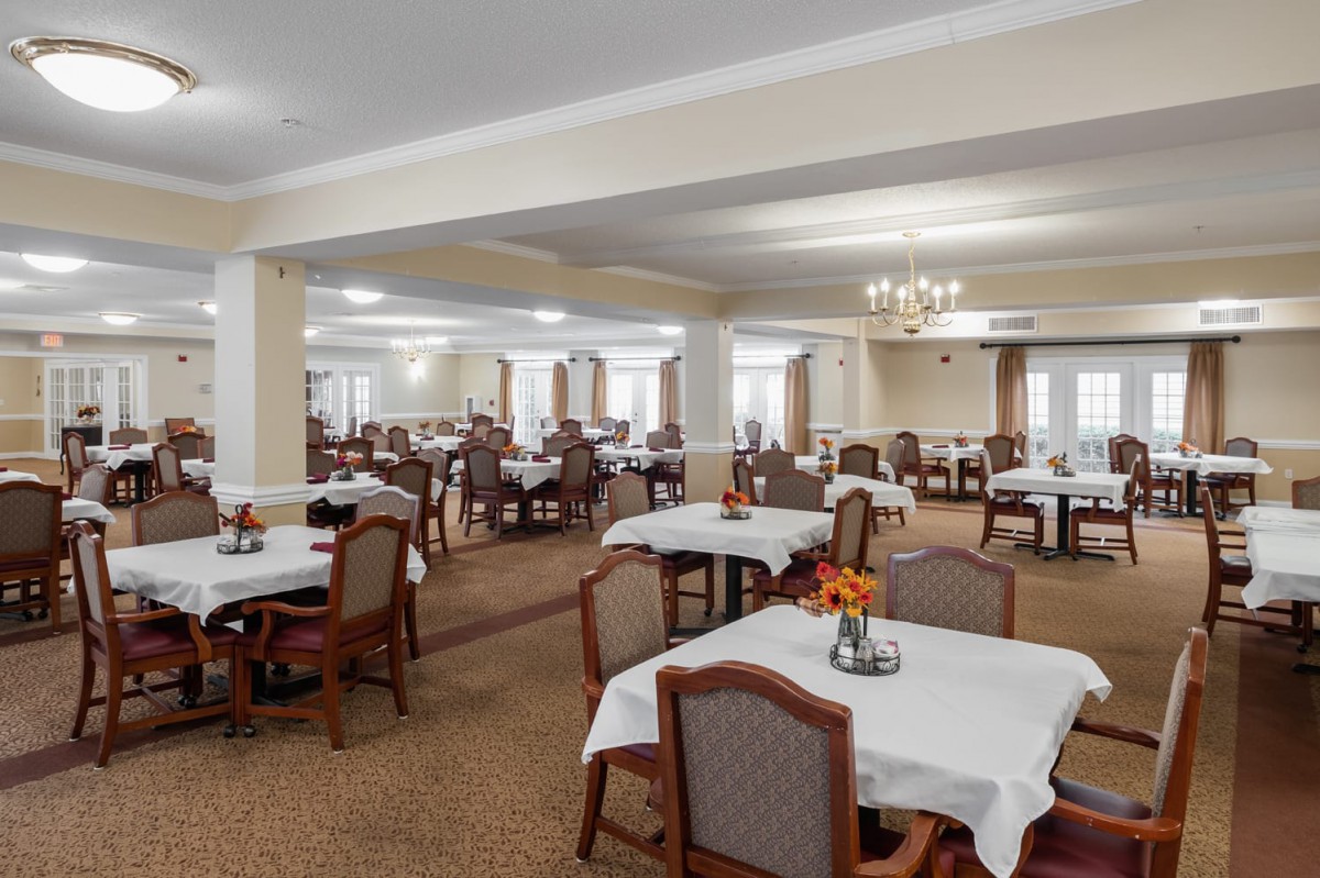 Spacious dining room with multiple tables and chairs, elegantly decorated with white tablecloths and a chandelier.