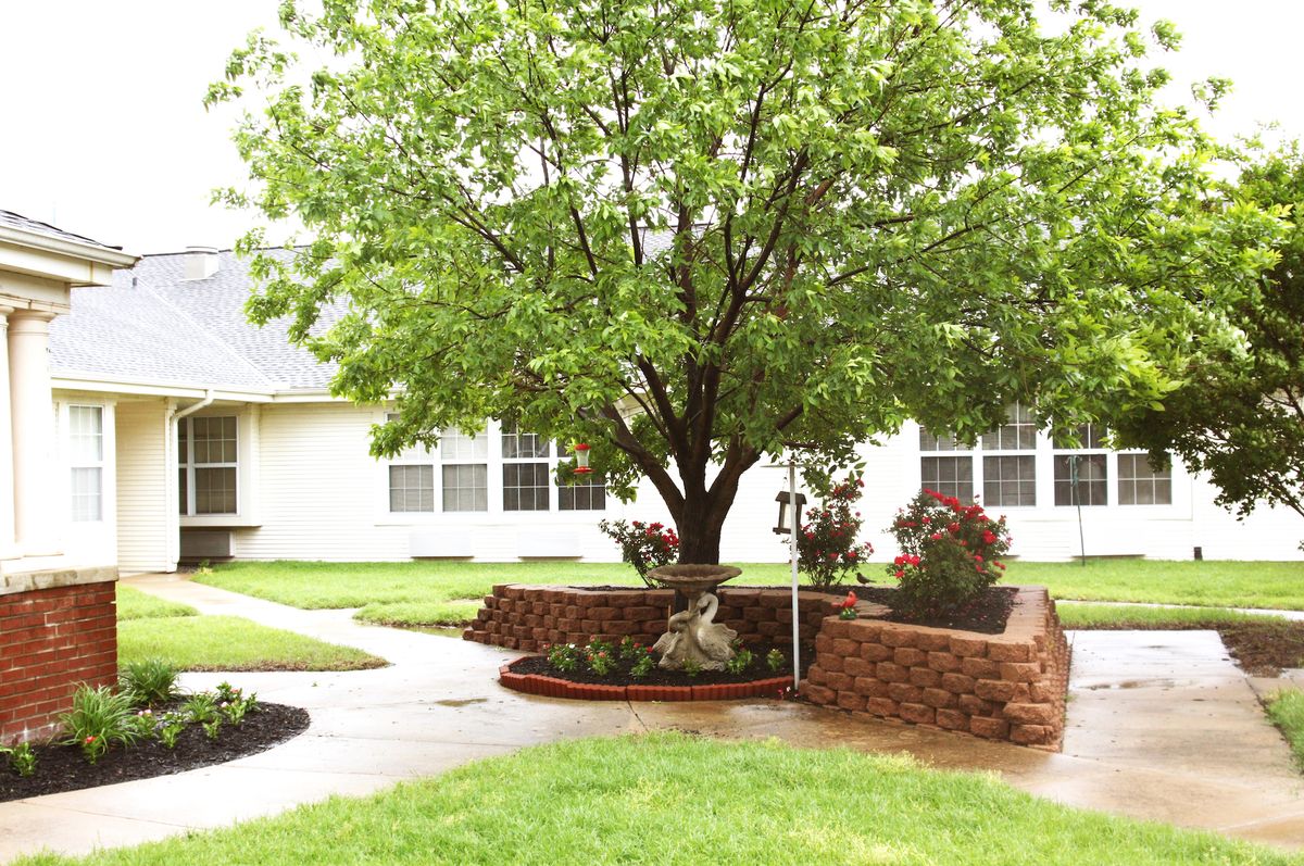 A landscaped garden featuring a large tree surrounded by a circular brick wall, with well-maintained lawns and pathways.