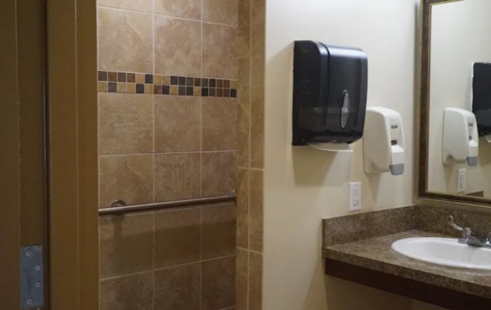 A bathroom with tiled walls, a paper towel dispenser, and a hand dryer.