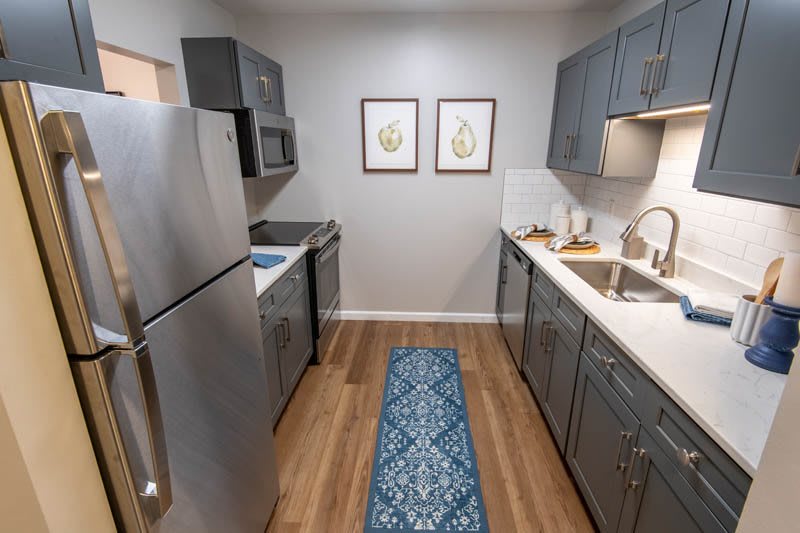 A modern kitchen with gray cabinets, stainless steel appliances, and wooden flooring.