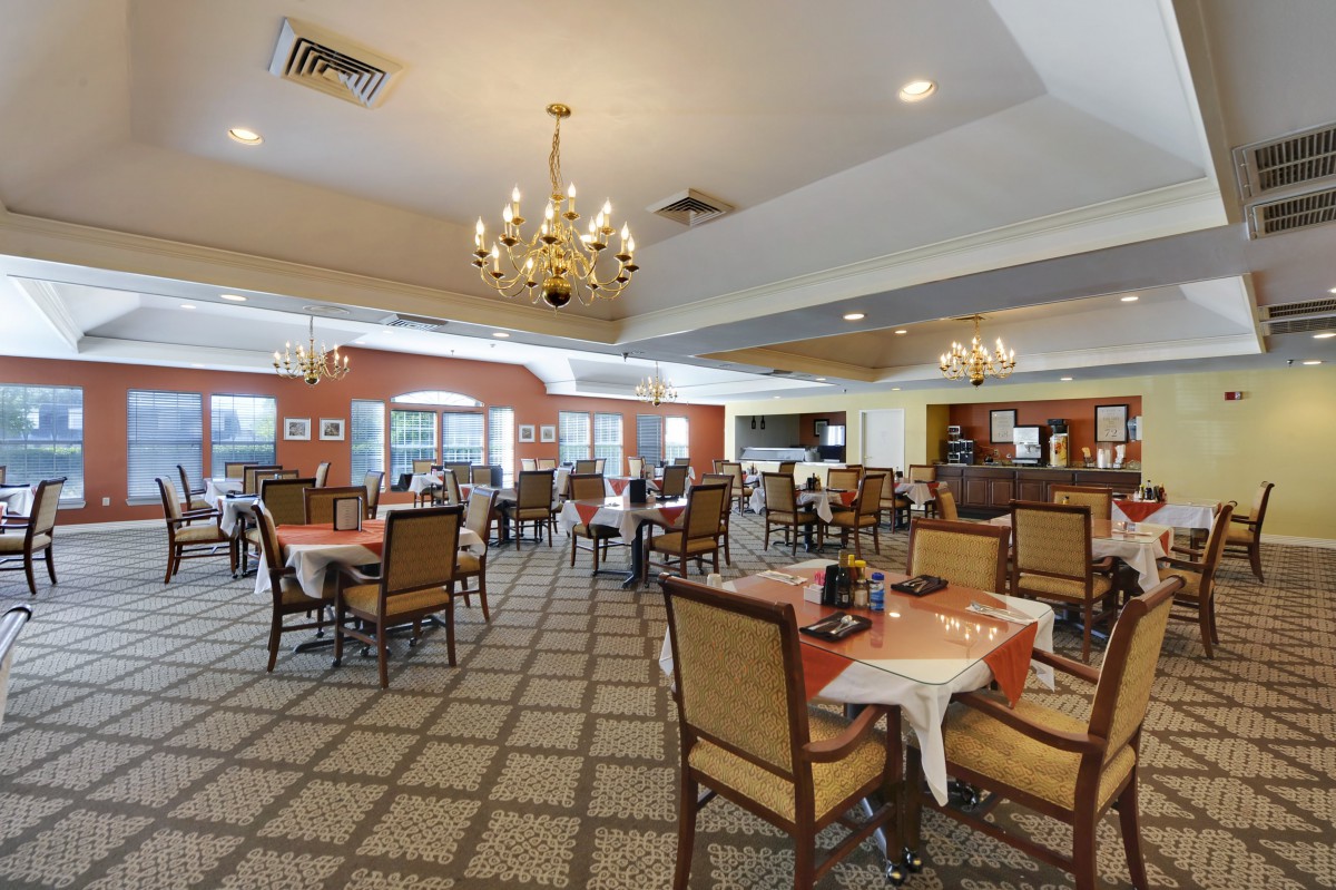 A spacious dining area with multiple tables and chairs, elegantly decorated with chandeliers.