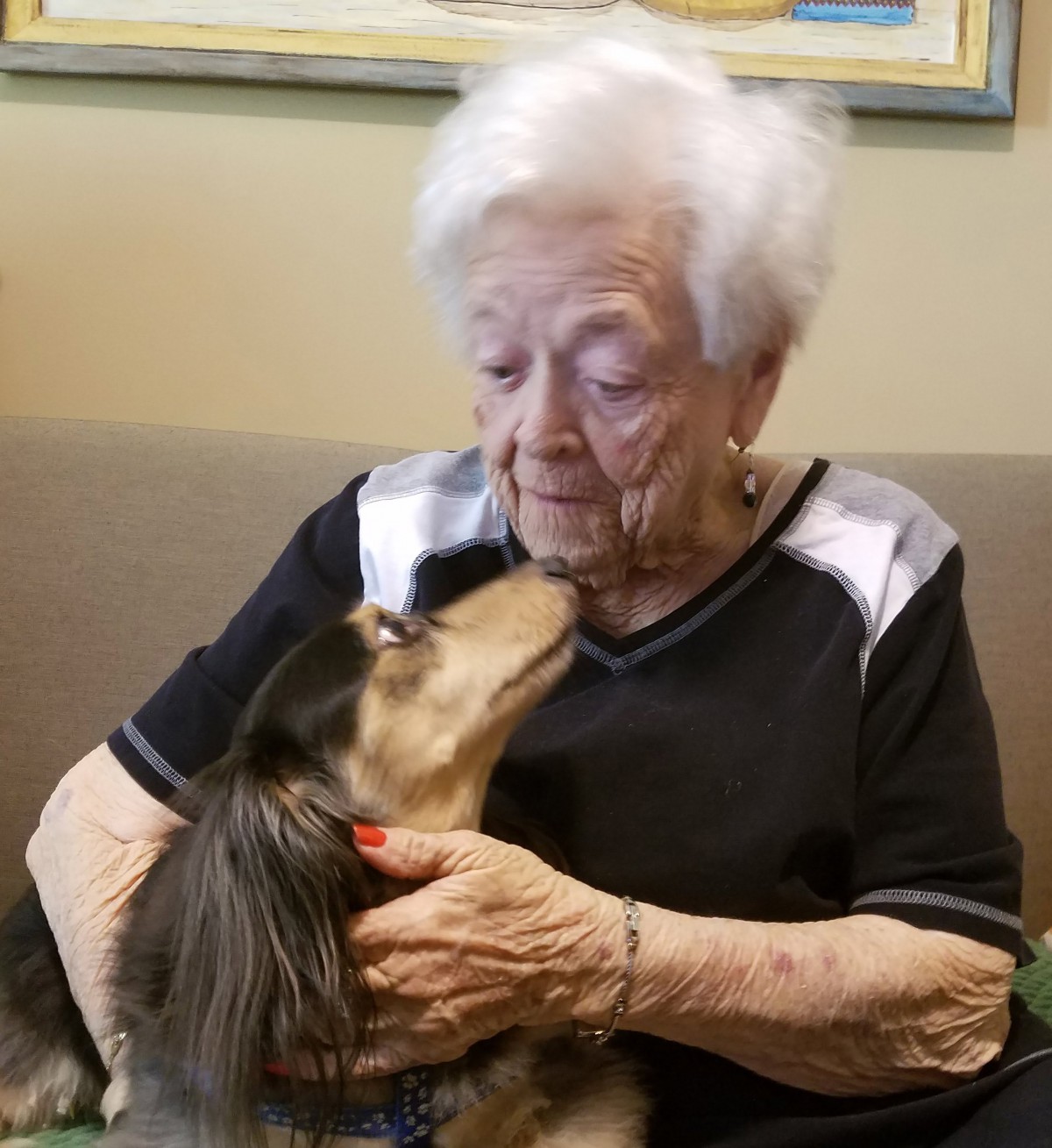 An elderly woman shares a tender moment with her dog indoors.