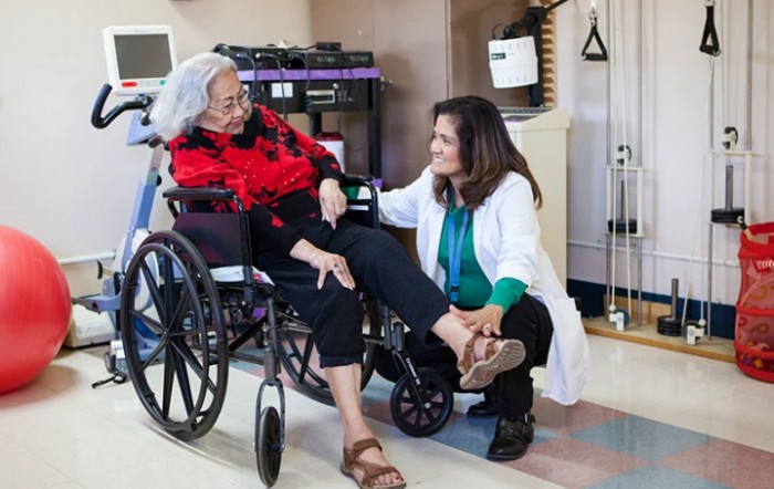 A healthcare professional assists an elderly woman in a wheelchair at a clinic.
