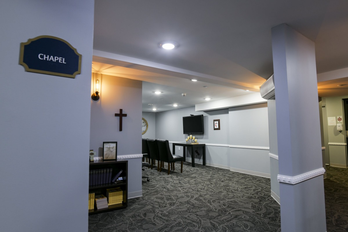 A small chapel interior with seating, a cross on the wall, and modern lighting.