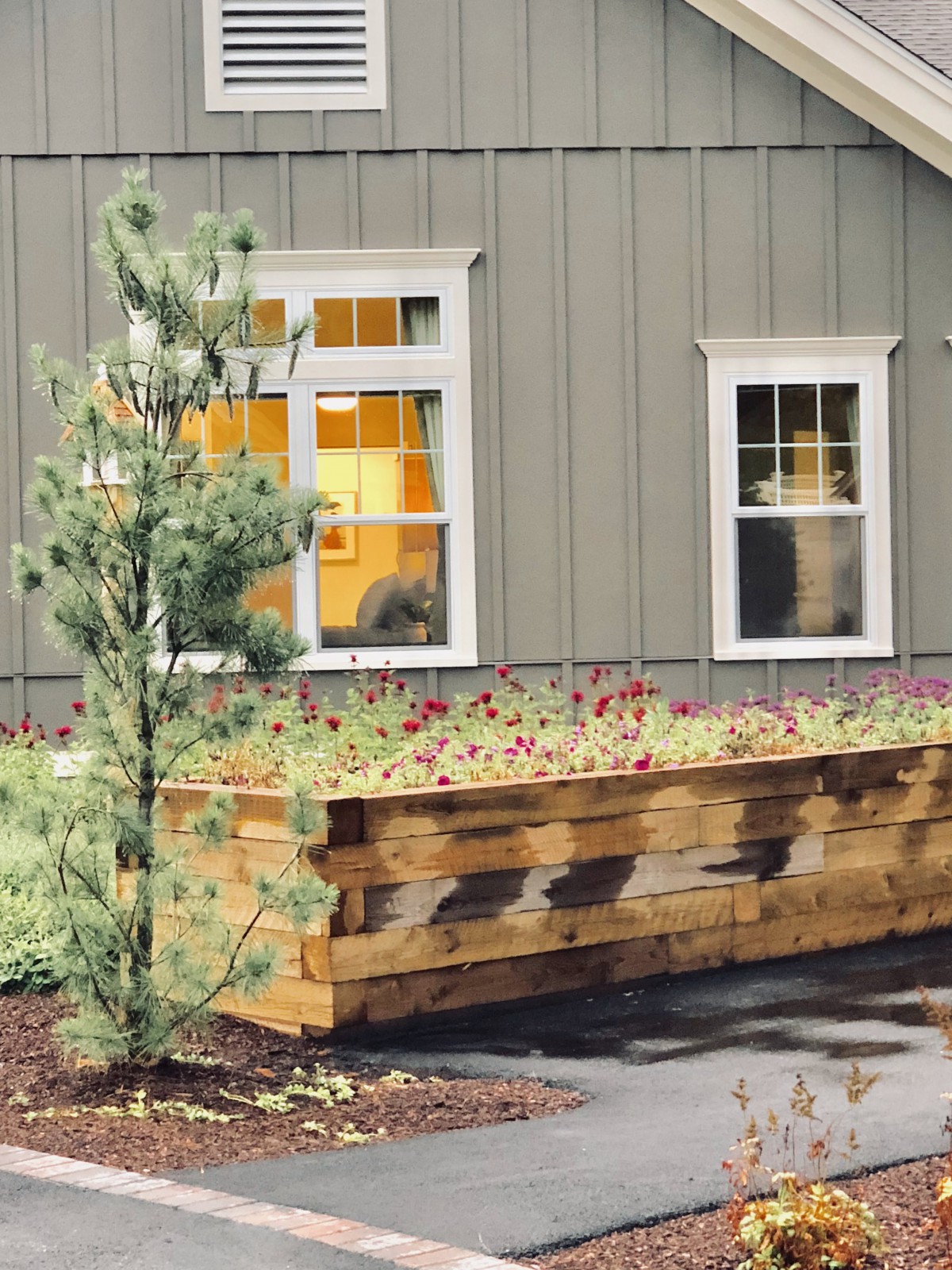 A quaint house with a large wooden planter box filled with flowers, accompanied by a small tree.