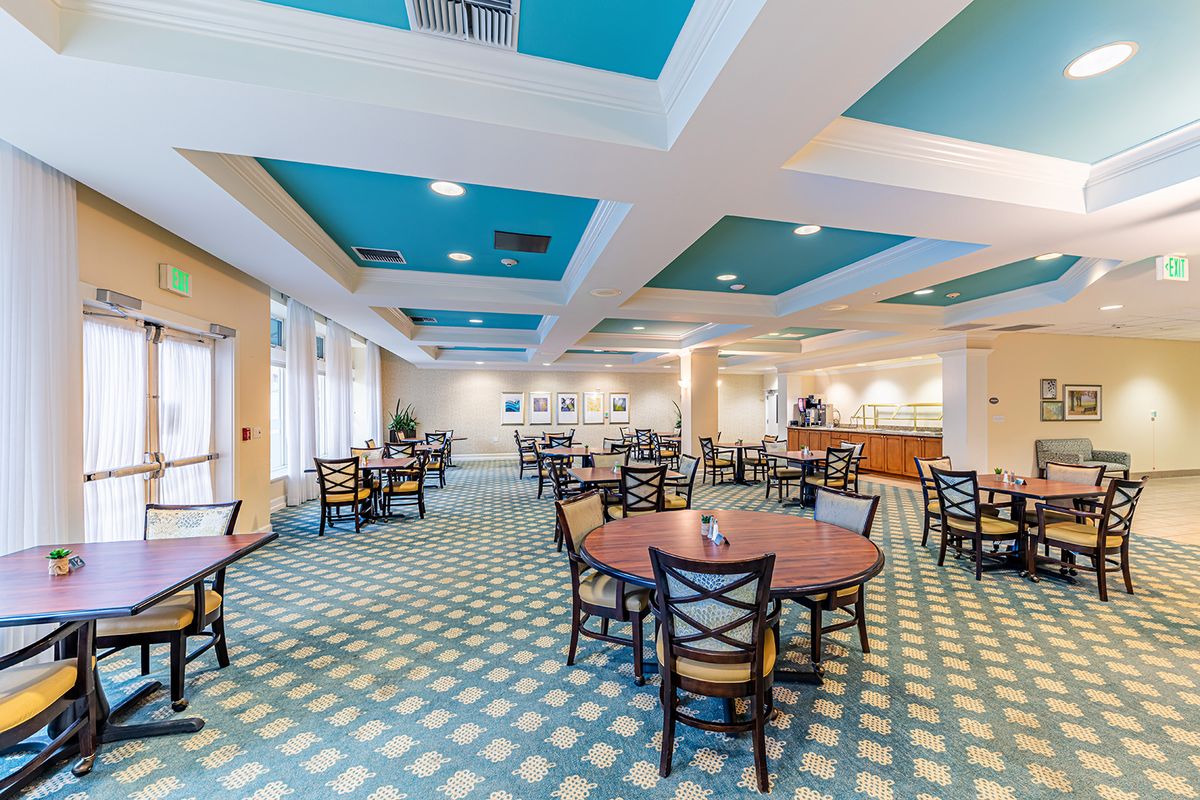 A spacious dining area with blue accents, featuring round tables and chairs arranged across a patterned carpet.