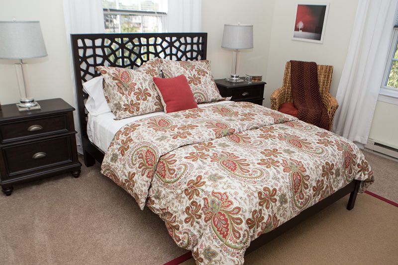 A cozy bedroom with patterned bedding and decorative pillows, featuring a modern headboard and bedside tables with lamps.