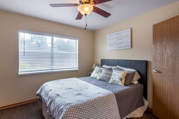 A cozy bedroom with a bed, bedside lamp, and ceiling fan.