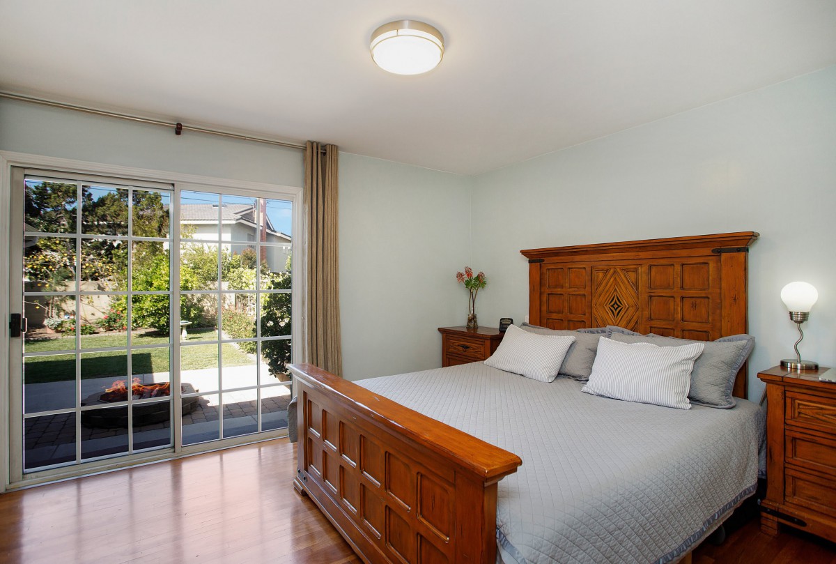 A cozy bedroom with a wooden bed frame and sliding glass doors opening to a garden view.