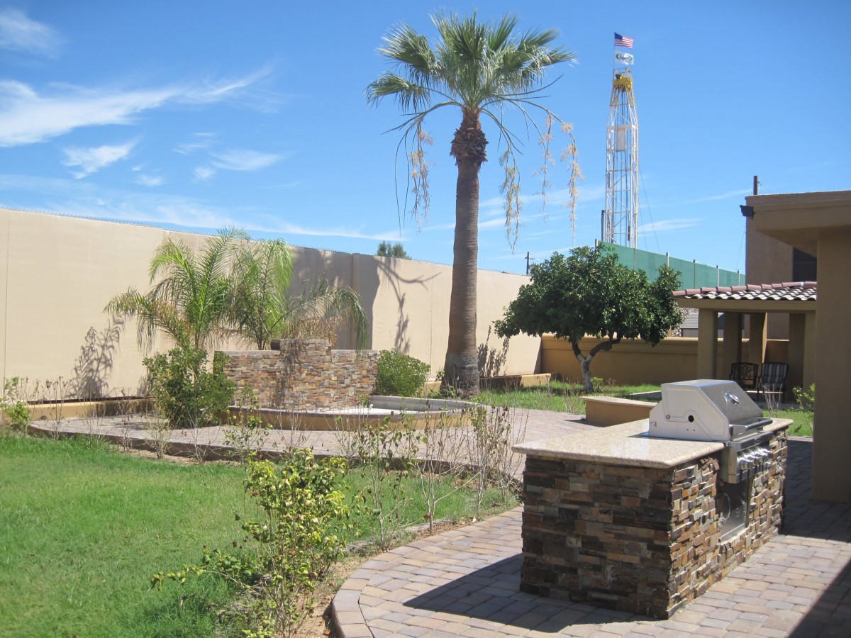A sunny outdoor patio with a barbecue grill and palm trees.