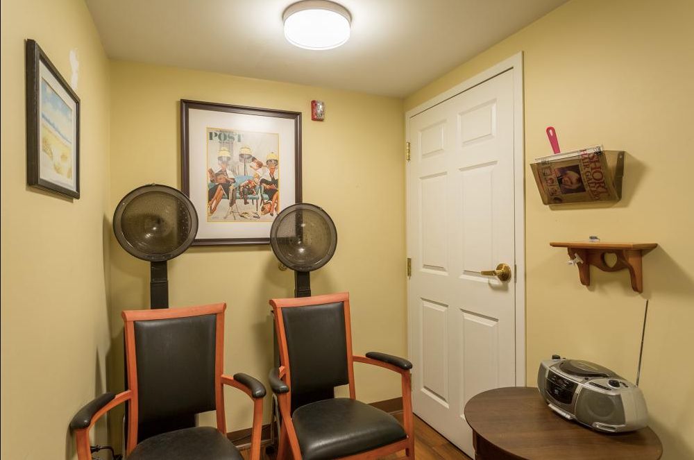 A cozy waiting room with chairs, fans, and a painting on the wall.