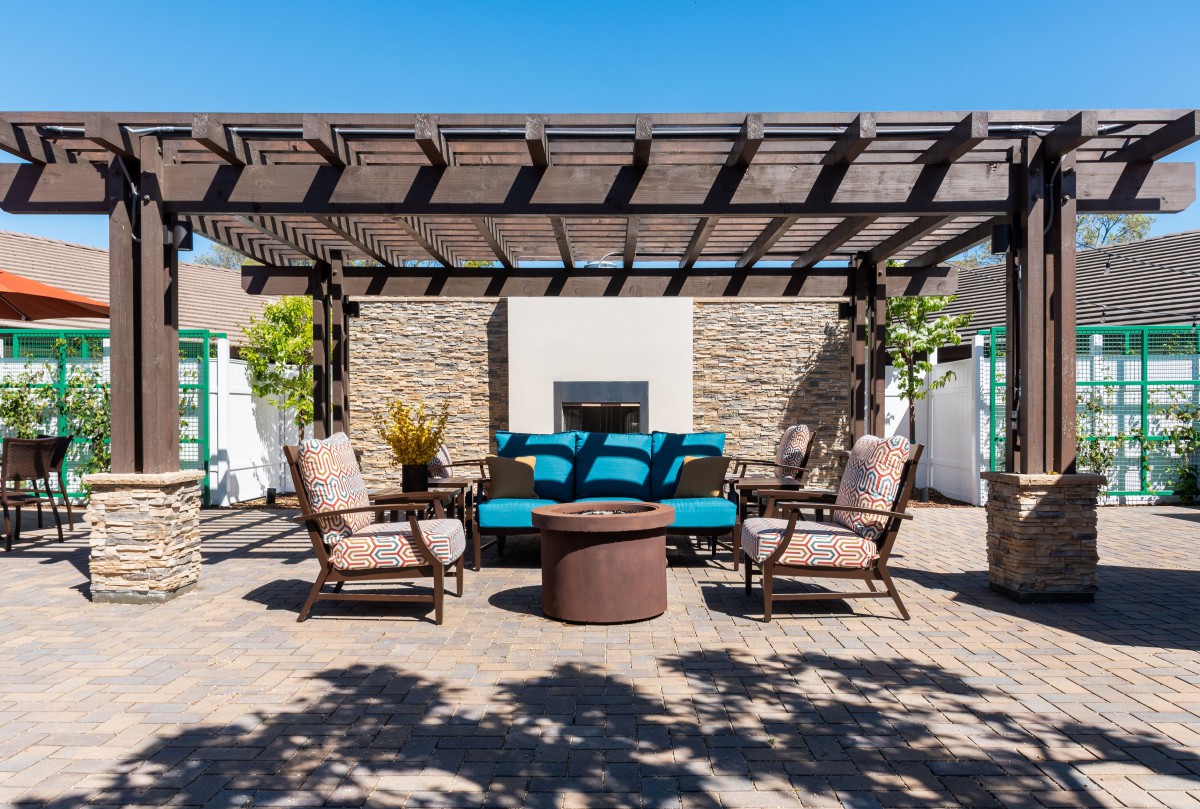 A cozy outdoor patio setup with a pergola, comfortable seating, and a central fireplace.