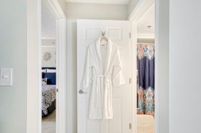 A white bathrobe hangs on a door between a bedroom and bathroom.