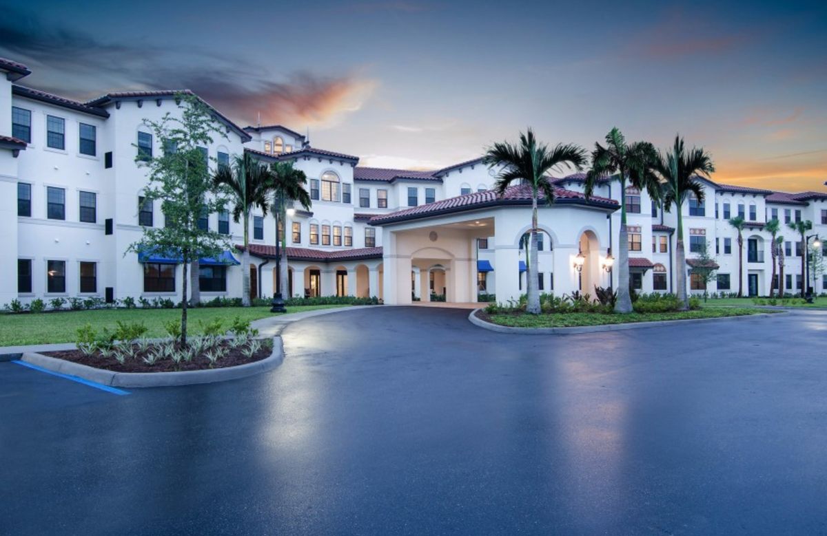 A majestic building with palm trees lining the entrance at sunset.