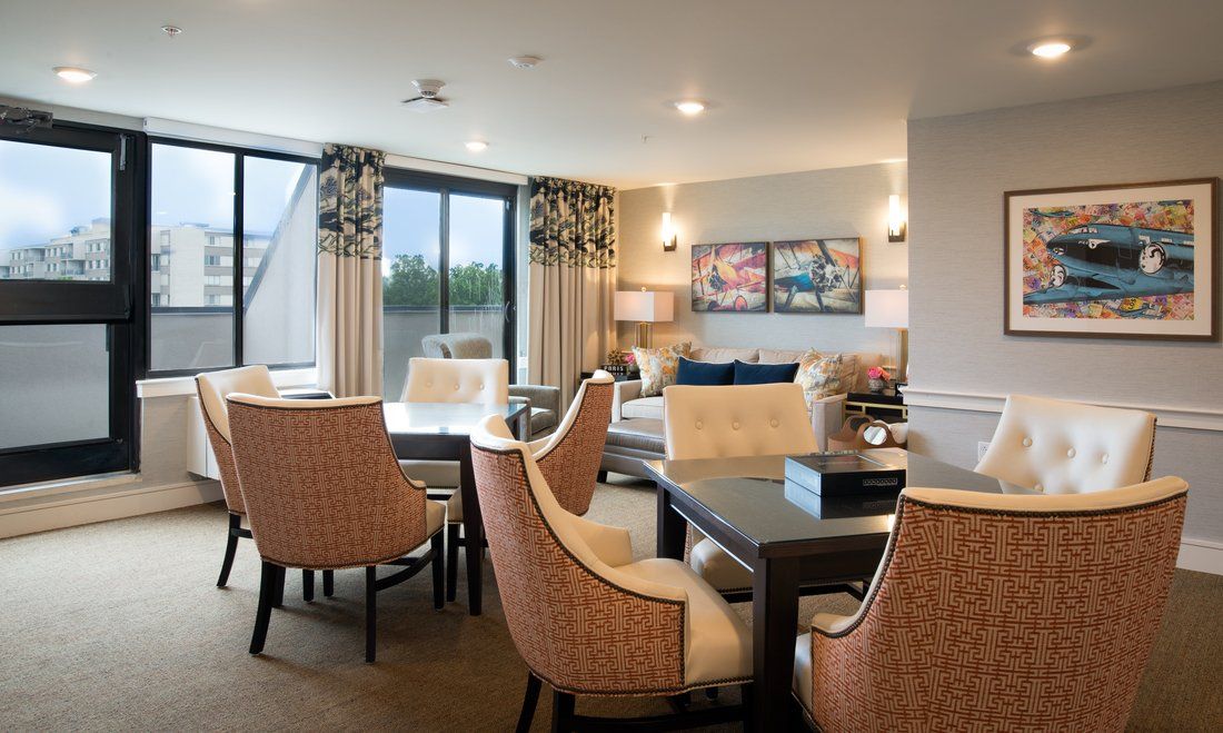 A modern and elegantly decorated living room with a dining area, featuring comfortable chairs and large windows.