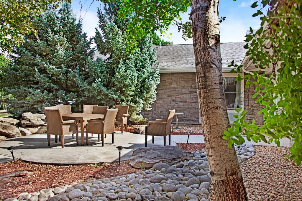 A tranquil backyard patio area with outdoor seating and lush trees.
