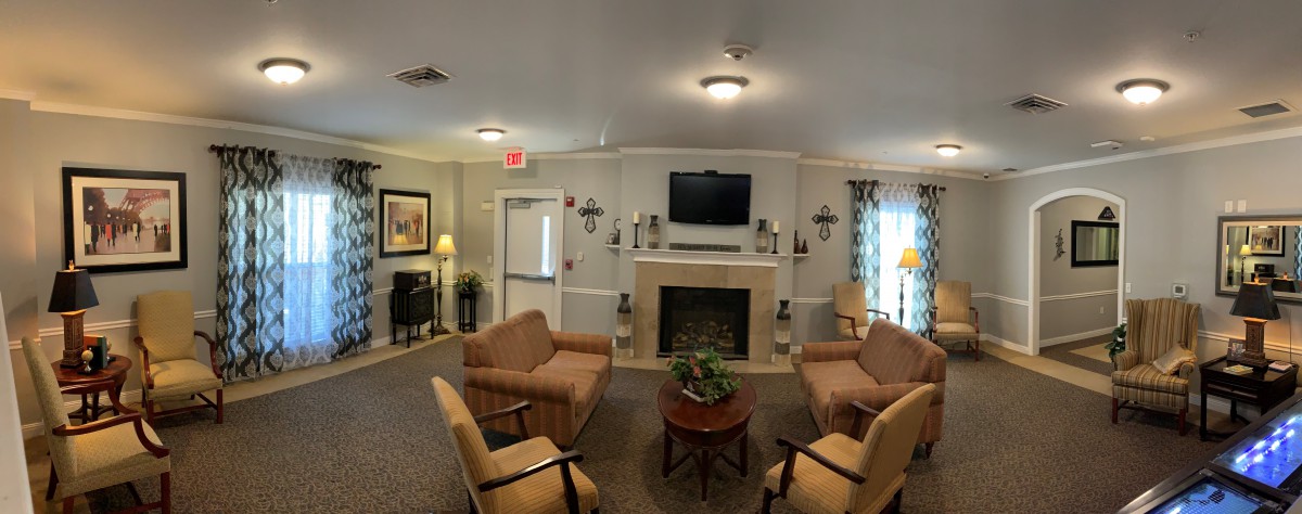 A cozy living room with four armchairs arranged around a central coffee table, featuring a fireplace with a television mounted above it.
