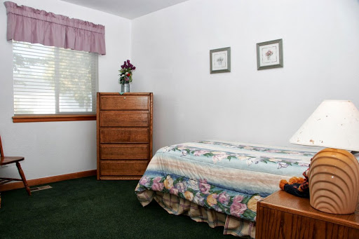 A cozy and simple bedroom featuring a floral bedspread, wooden dresser, and green carpeting.