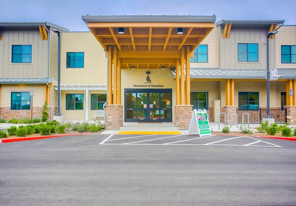 Front entrance of a modern building with wooden accents and a parking area.