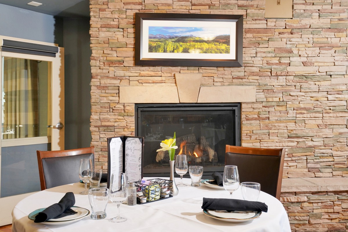 A cozy restaurant setting featuring a neatly arranged dining table in front of a warm fireplace.