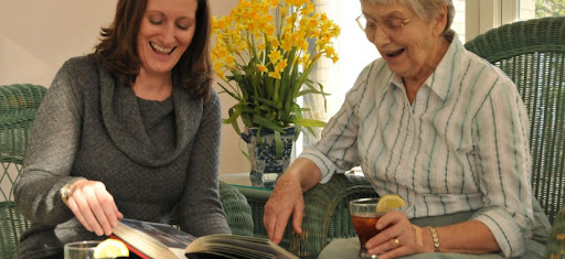 A joyful moment between two women as they share memories over a photo album, surrounded by vibrant flowers.