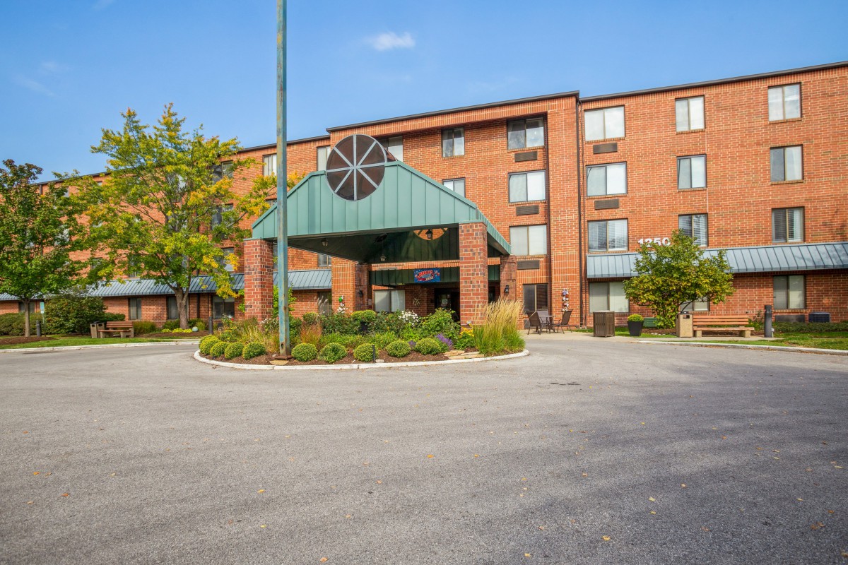 The image shows the exterior of a hotel with a landscaped entrance area.