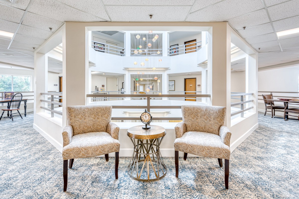 A modern lobby with two chairs and a small table, overlooking an open atrium filled with natural light.