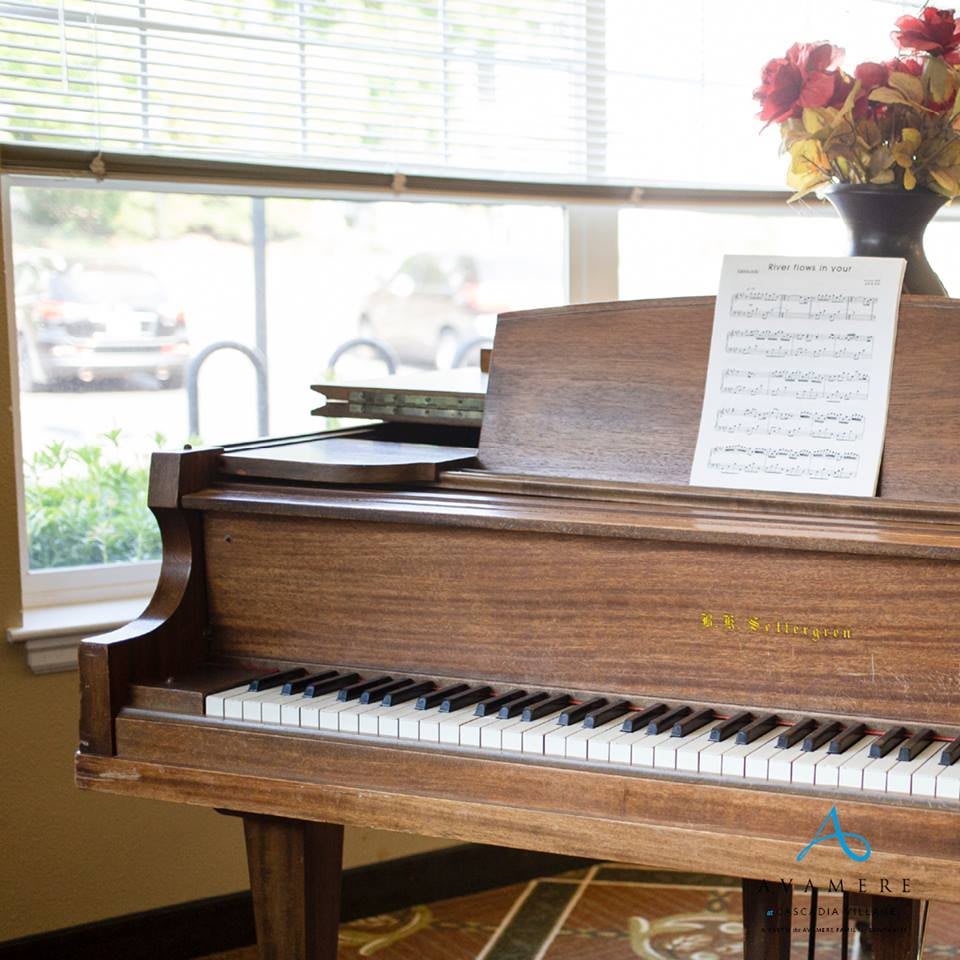 A wooden piano with sheet music and flowers by the window.