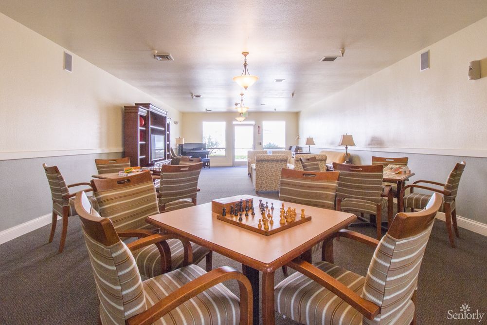 A cozy living room with a chessboard on the table surrounded by striped chairs and a bookshelf in the background.